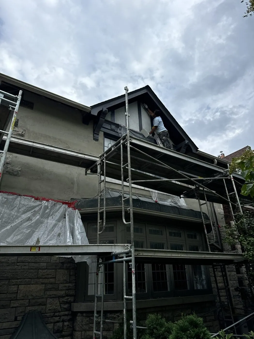 Stucco being applied by hand to a Tudor gable from scaffolding, with windows masked off
