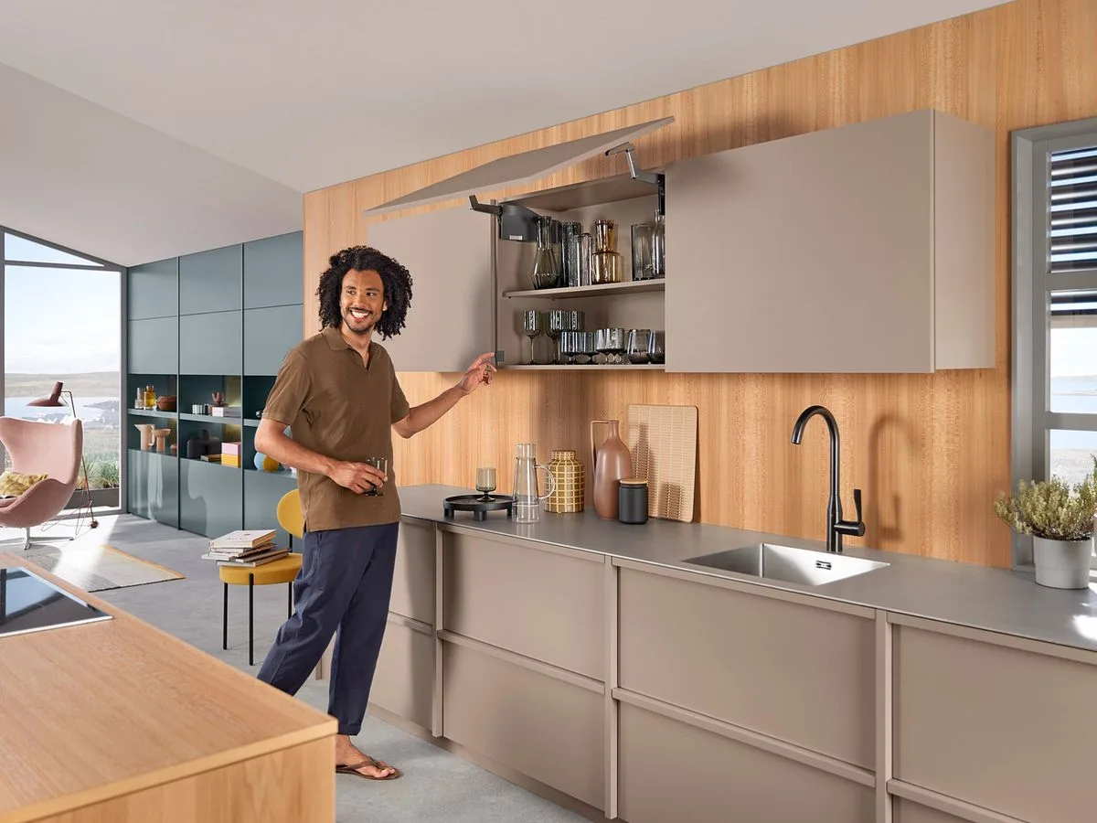 Homeowner opening a Blum AVENTOS lift-up upper cabinet door in a modern kitchen